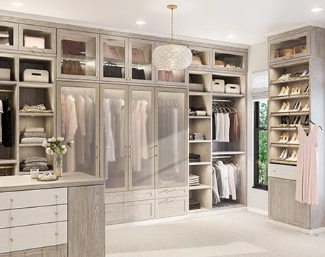 Custom walk in closet design with extra shelving, shoe storage, island, lighted glass cabinets by California Closets